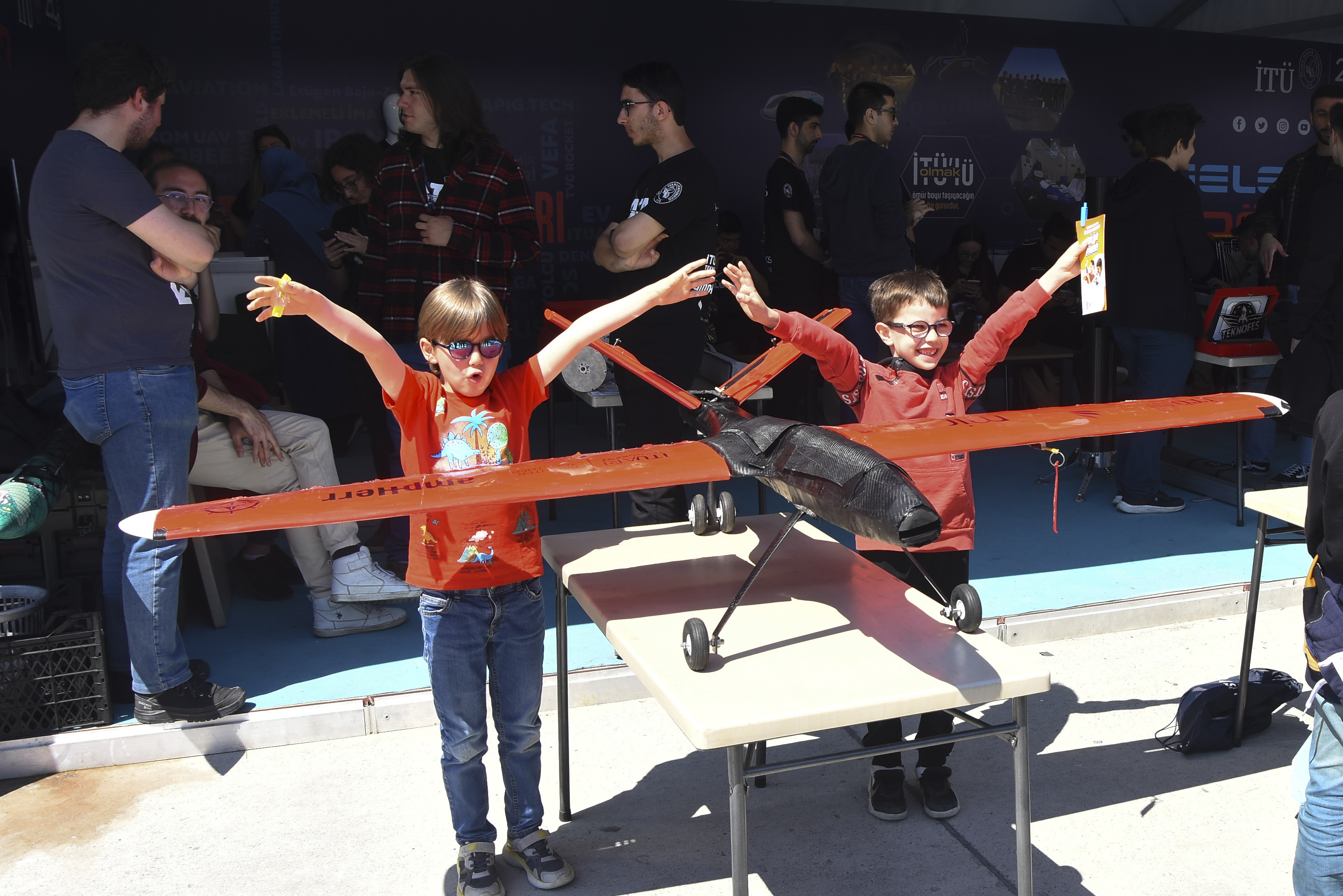 Ödül kazanan İTÜ ATA insansız hava aracının kanatları hizasında kollarını iki yana açarak kartal duruşuyla gülümseyen iki küçük çocuk